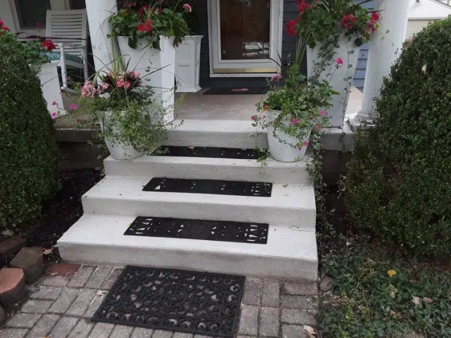 Beautiful new concrete walkway and steps leading into home with flowers and mats