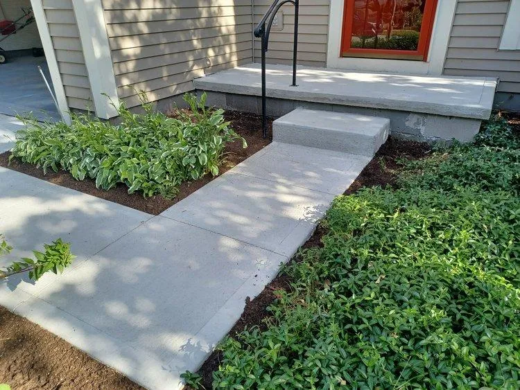 Perfectly installed new concrete walkway leading into house in Dublin with plants and red door